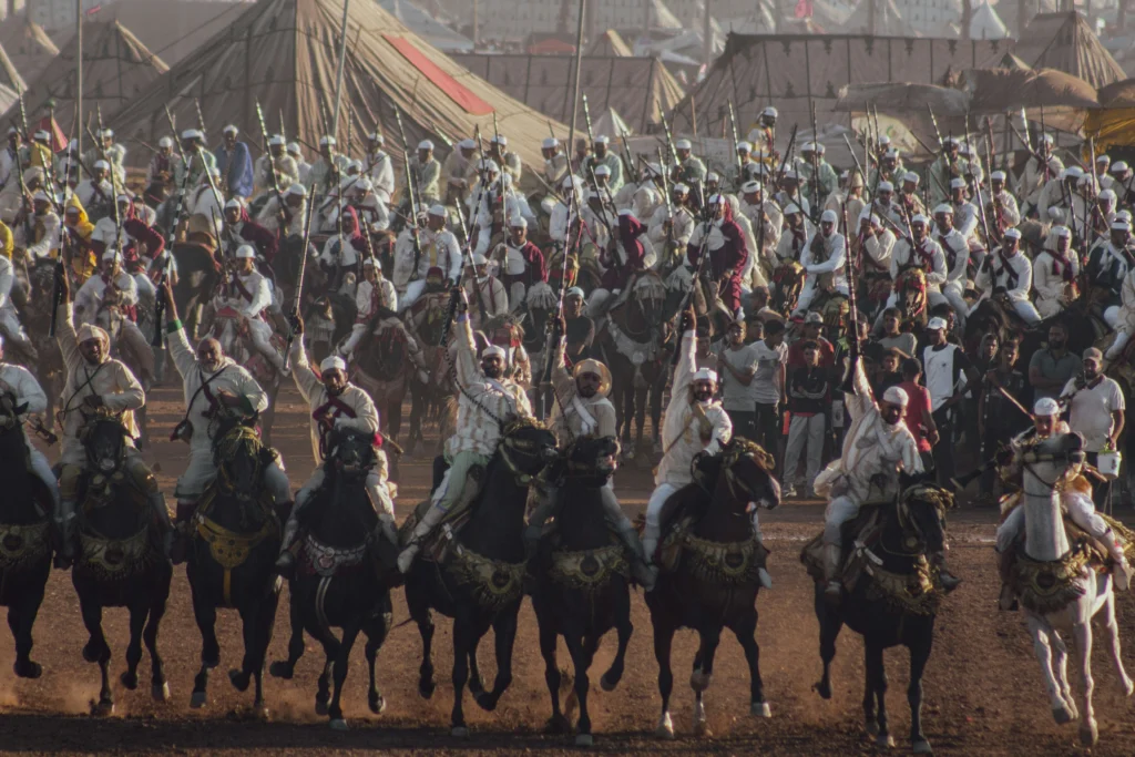 Moroccan riders in traditional clothing performing Tbourida fantasia on decorated horses while firing rifles simultaneously during a cultural festival in Morocco.